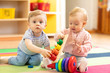 funny babies boy and girl playing on floor in game room in nursery