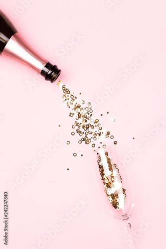 Golden confetti pouring from a bottle of champagne into a glass on pink backg...