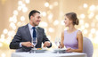 © Syda Productions - people and leisure concept - smiling couple eating appetizers at restaurant over festive lights on beige background