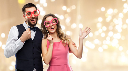 photo booth, fun and people concept - happy couple posing with party props over festive lights background