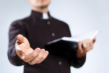 Young Priest Reading The Holy Bible And Stretching His Hand On Neutral Background