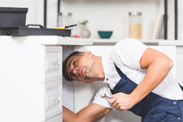 Wall Mural - adult repairman holding spanner while checking pipes at kitchen