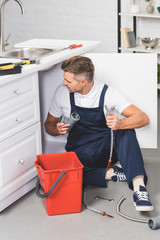 Wall Mural - adult repairman with red plastic bucket holding pipes for repairing kitchen sink