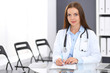 © rogerphoto - Doctor woman at work. Portrait of female physician filling up medical form while sitting at the glass desk at clinic or hospital. Medicine and healthcare concept