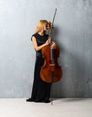 Wall Mural - Young blonde girl with her cello on textured wall background