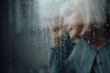 © LIGHTFIELD STUDIOS - blurred portrait of lonely senior woman at home through window with raindrops