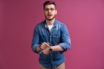 Portrait of a shocked man looking on wrist watch over pink background.