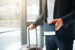 © estradaanton - Cut view of man in suit stand at window in airport. He hold passport with ticket in it and suitcase with another hand.