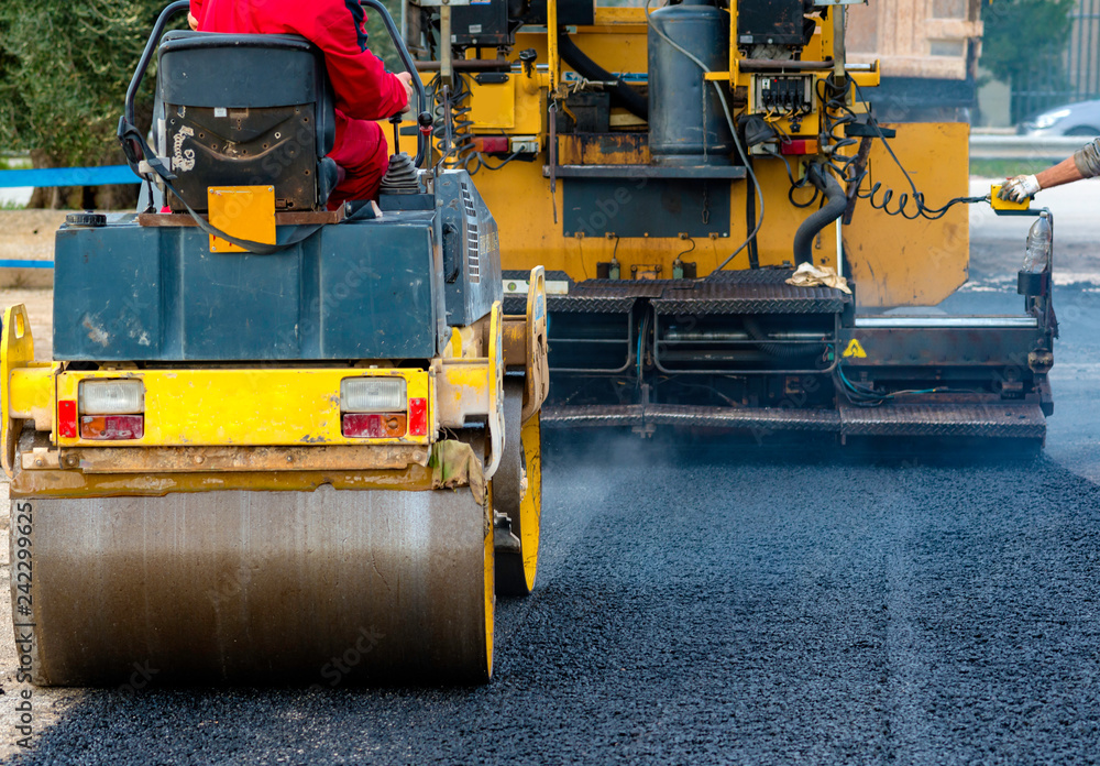 Worker leads the vibrating road roller to compact the asphalt laid out for the construction of a road