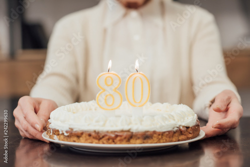 Plakat częściowy widok starszy kobieta trzyma tort urodzinowy z numerem 80 na górze w domu