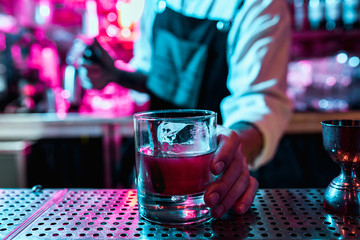 Expert barman is making cocktail at night club or bar. Glass of fiery cocktail on the bar counter against the background of bartenders hands with fire. Barman day concept