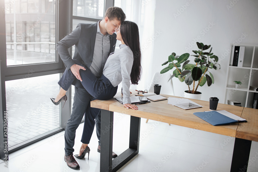 Sexual and intimate picture of couple at work. She sit on table. He