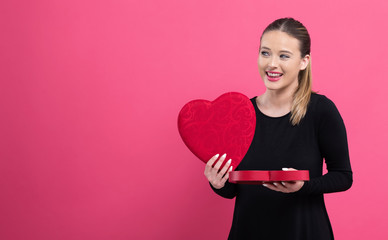 Wall Mural - Young woman holding a big heart gift box on a pink background