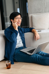 Sticker - Happy asian man sitting on a couch at home