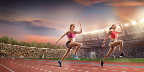 Female athletes sprinting. Two women in sport clothes run at the running track in professional stadium