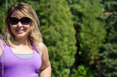 Fotografie, Obraz Portrait of a young adult woman wearing sunglasses and smiling next to a rocky b