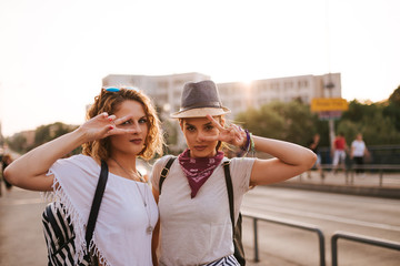 Wall Mural - Close-up image of two beautiful party girls showing the peace sign in the sunset.