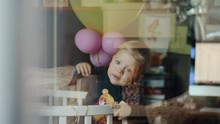View Through The Window To One Year Old Baby Girl Standing In Crib With Balloon