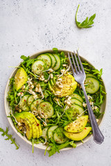 Wall Mural - Healthy green salad with avocado, cucumber and arugula in white dish, top view, copy space.