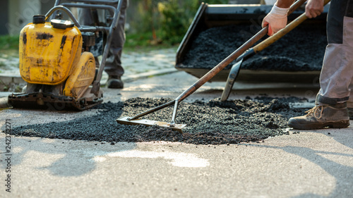 Cuadros en Lienzo Low angle view of two workers arranging fresh asphalt mix with rakes and shovel