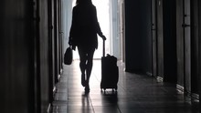 Tilt Up Of Silhouette Of Unrecognizable Businesswoman Carrying Briefcase And Pulling Luggage While Walking Along Hallway In Hotel