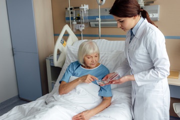 female doctor giving pills to senior woman lying in hospital bed