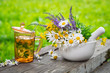 Healthy herbal tea cup, mortar of medicinal herbs on wooden board outdoors.