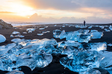 Diamond Beach in Iceland with blue icebergs melting on the black sand and ice glistening with sunrise sun light, tourist looking at beautiful arctic nature scenery, Icelandic South coast, Jokulsarlon