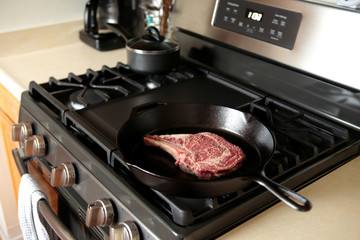 Rib eye steak cooking in a cast iron pan on a natural gas stove top.
