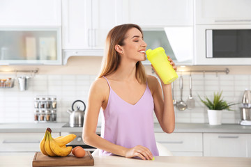 Canvas Print - Young woman drinking protein shake near table with ingredients in kitchen