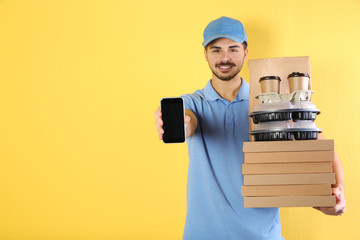 Canvas Print - Young man holding orders and smartphone on color background, mockup for design. Online food delivery