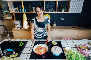 Smiling woman cooking a healthy meal in home kitchen.Making dinner on kitchen island.Preparing chicken,enjoying spice aromas.Eating in.Passion for cooking.Healthy lifestyle and dieting concept.