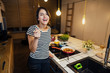 © eldarnurkovic - Young woman tasting a healthy meal in home kitchen.Making dinner on kitchen island standing by induction hob.Preparing fresh vegetables,enjoying spice aromas.Eating in.Passion for cooking.Dieting