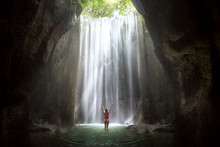 Woman With Arms Raised To Gorgeous Scenic Epic Majestic Waterfall In Cave With Light Rays