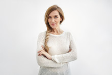 Confident Senior Woman Wearing Elegant Sweater And Long Braid Crossing Arms, Smiling. Attractive Stylish Mature Female With Green Eyes And Wrinkles Posing At Blank Wall With Copy Space For Your Text