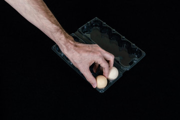 Male hand taking one egg from plastic egg box on black mat background