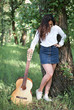 © soleg - young woman walking in the forest and playing guitar, summer nature, bright sunlight, shadows and green leaves, romantic feelings