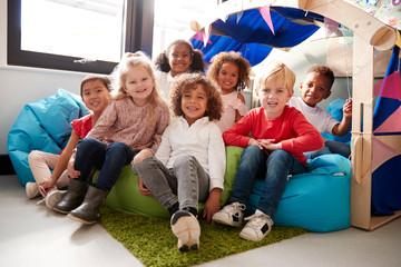 Poster - A multi-ethnic group of infant school children sitting on bean bags in a comfortable corner of the classroom, smiling to camera, low angle, close up