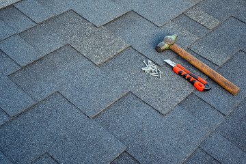 Close up view on asphalt bitumen shingles on a roof  with hammer,nails and stationery knife background.