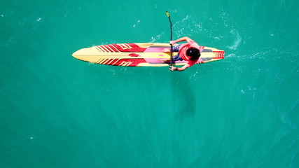 Aerial drone bird's eye view of young man exercising sup board in turquoise tropical clear waters