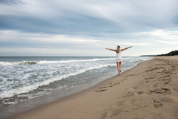 Woman on the beach / Rear view of a beautiful young woman in white dress jumping on the sandy beach