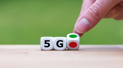 Green light for 5G (fith generation wireless). Hand is turning a dice and changes the color of a dot from red to green symbolizing the start of 5G.