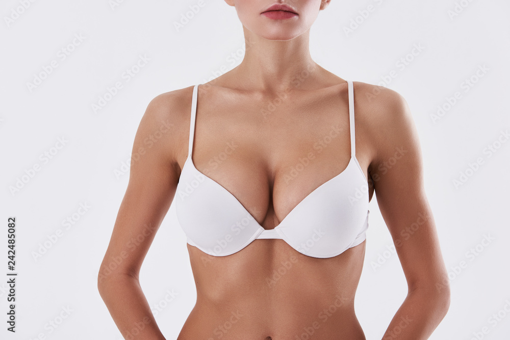 Attractive lady with beautiful breast in bra standing against white background - obrazy, fototapety, plakaty 