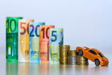 Blurred Row Of Rolled Hundred, Fifty, Twenty, Ten And Five New Euro Banknotes And Pile Of Coins With Yellow Toy Expensive Sport Car. Symbol Of Financial Prosperity, Vehicle Sale And Purchase.