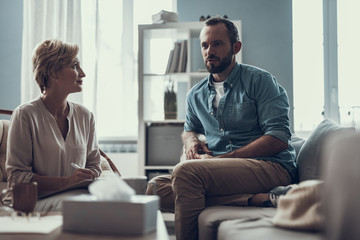 Wall Mural - Calm psychotherapist looking at the bearded man sitting and talking