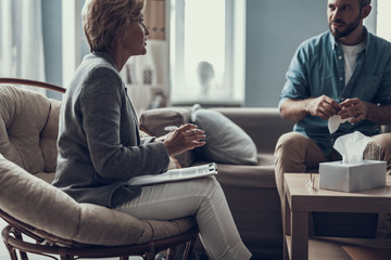 Wall Mural - Bearded man holding paper tissue and his psychotherapist talking