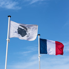 French And Corsican Flags Fluttering In The Wind Against A Blue Sky With Clouds