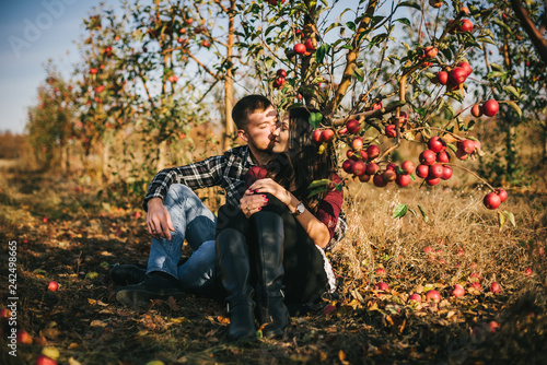 Fotografie, Obraz Young beautiful couple sitting on the grass under an apple tree, outdoor