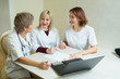 © Alexandr - three women doctor in white coats sit at the table in the clinic in the office with a laptop