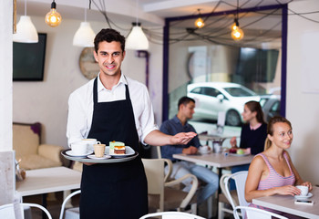 Waiter holding served tray meeting visitors at pastry bar